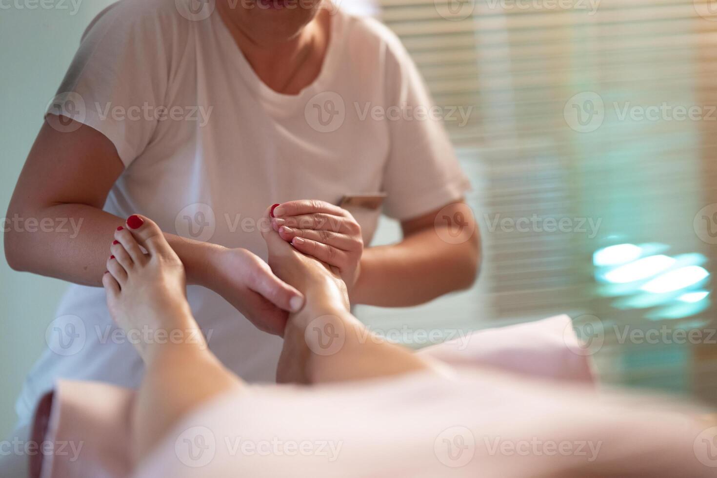 Foot Massage Therapy in a Relaxing Spa Setting. A professional massage therapist in a white uniform provides a soothing foot massage to a client in a calm and serene spa environment photo