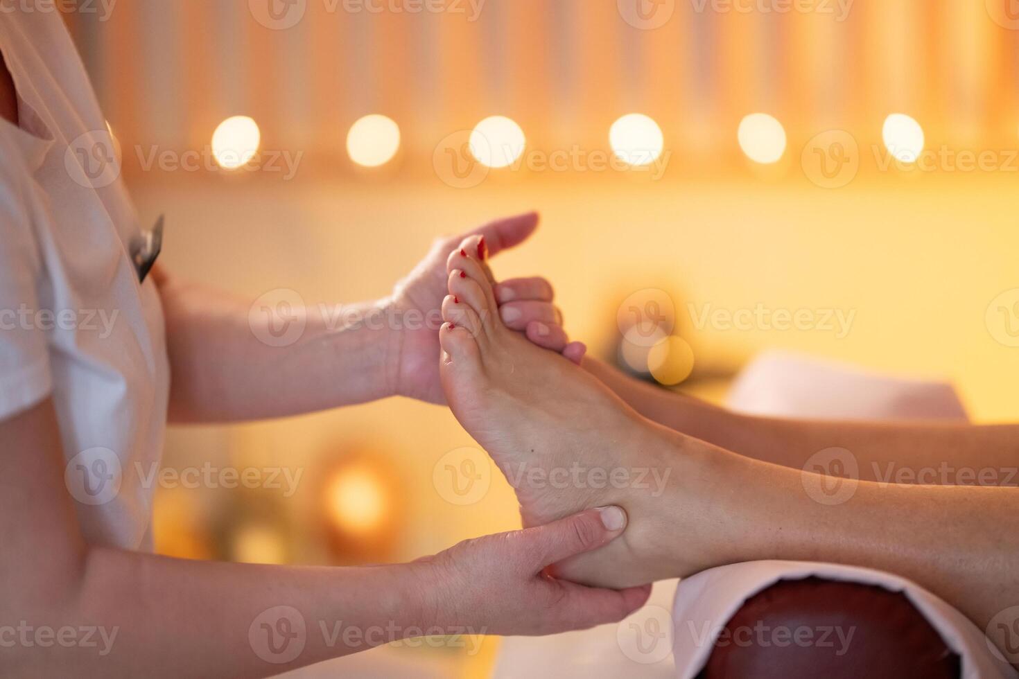 Foot Massage Therapy in a Relaxing Spa Setting. A professional massage therapist in a white uniform provides a soothing foot massage to a client in a calm and serene spa environment photo