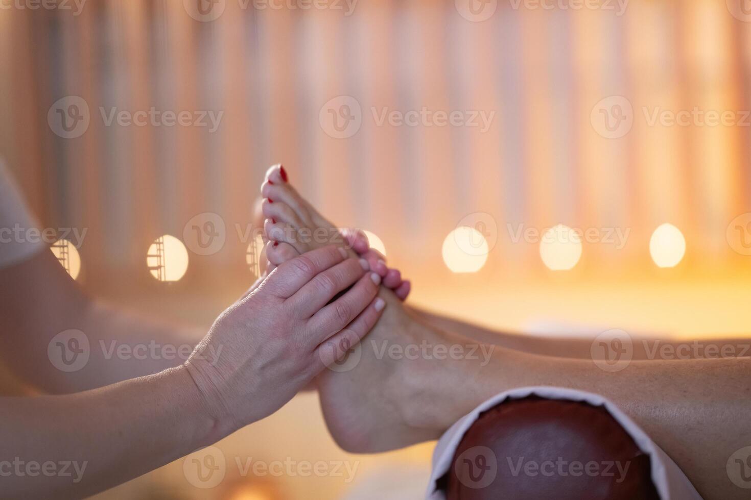 Foot Massage Therapy in a Relaxing Spa Setting. A professional massage therapist in a white uniform provides a soothing foot massage to a client in a calm and serene spa environment photo