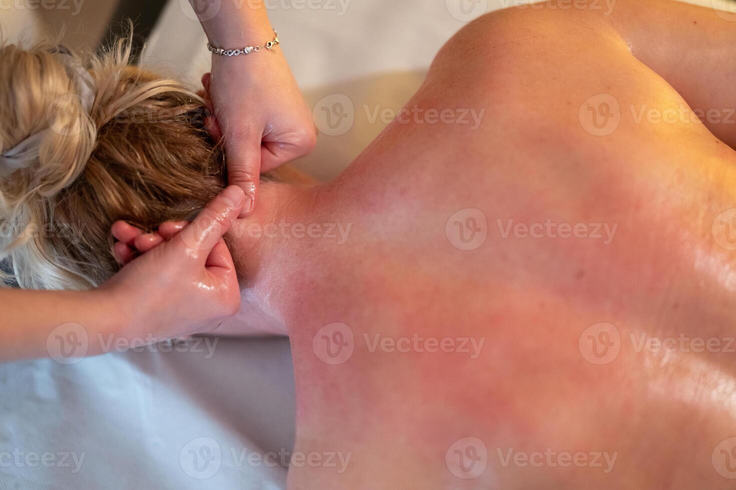 Relaxing Back Massage in a Spa Setting. A professional massage therapist in a blue uniform provides a relaxing back massage to a client lying on a massage table. photo