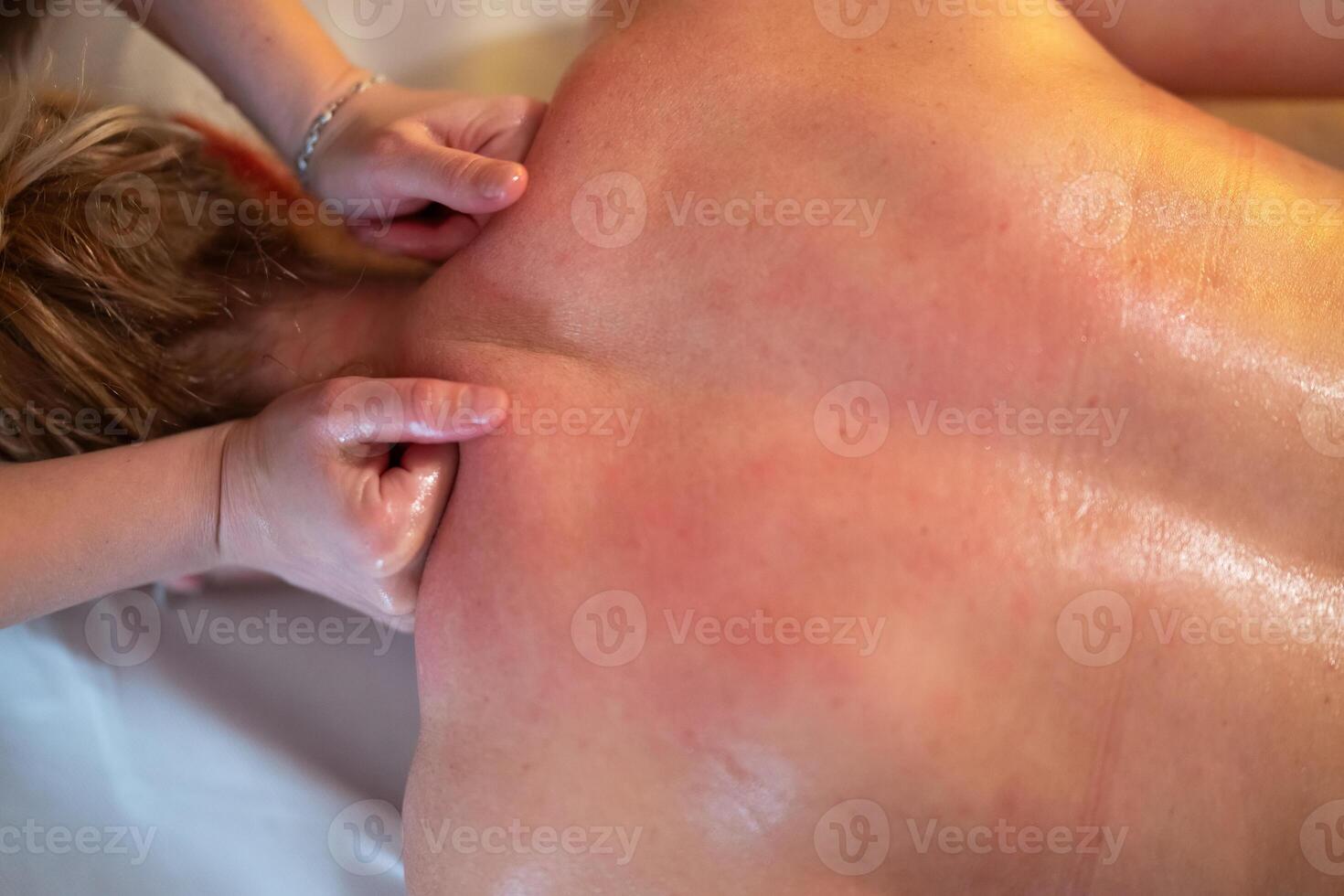 Relaxing Back Massage in a Spa Setting. A professional massage therapist in a blue uniform provides a relaxing back massage to a client lying on a massage table. photo