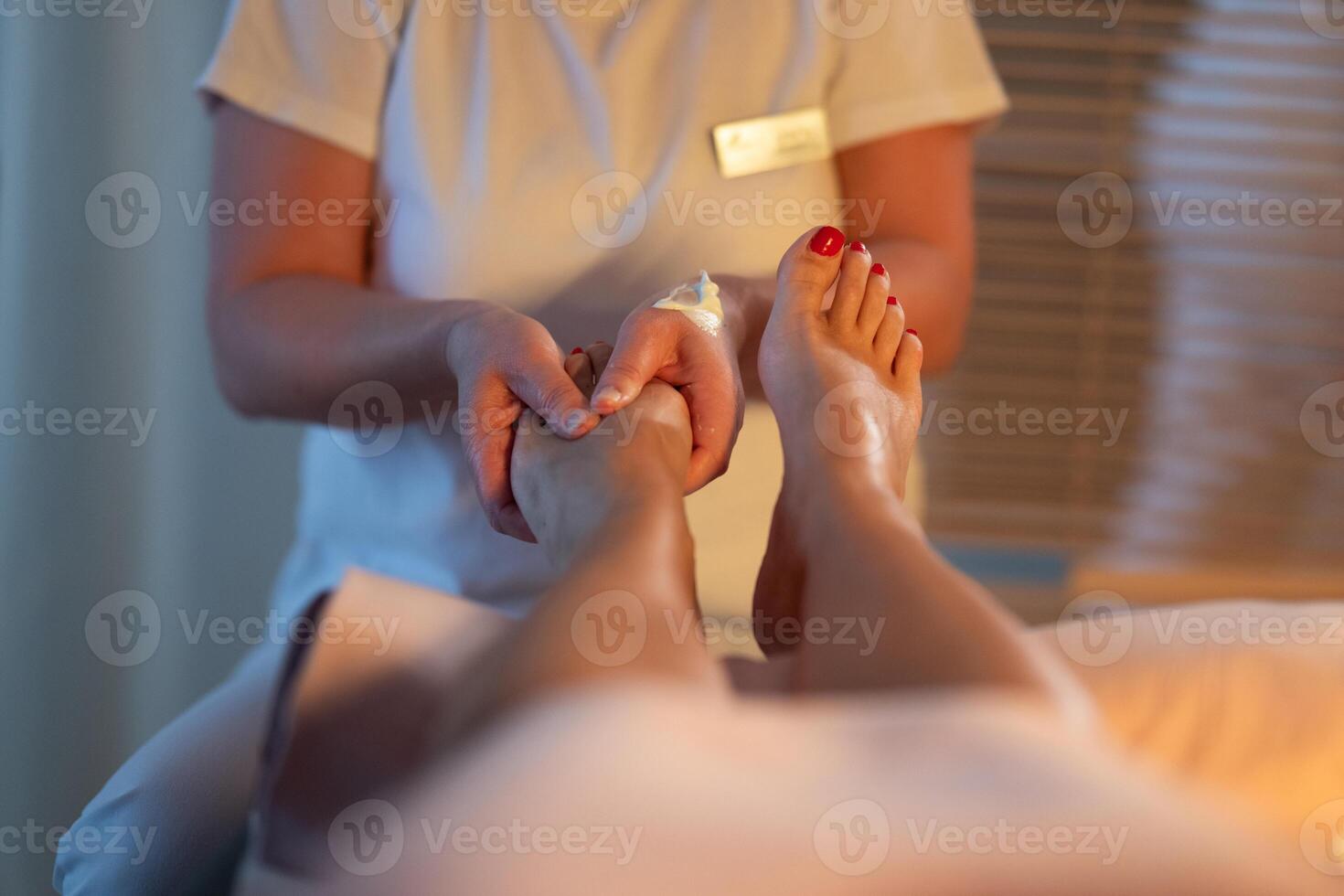 Foot Massage Therapy in a Relaxing Spa Setting. A professional massage therapist in a white uniform provides a soothing foot massage to a client in a calm and serene spa environment photo
