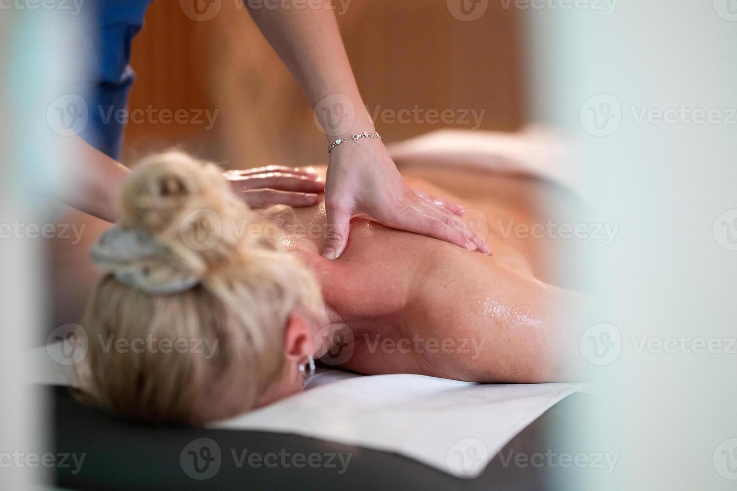 Relaxing Back Massage in a Spa Setting. A professional massage therapist in a blue uniform provides a relaxing back massage to a client lying on a massage table. photo
