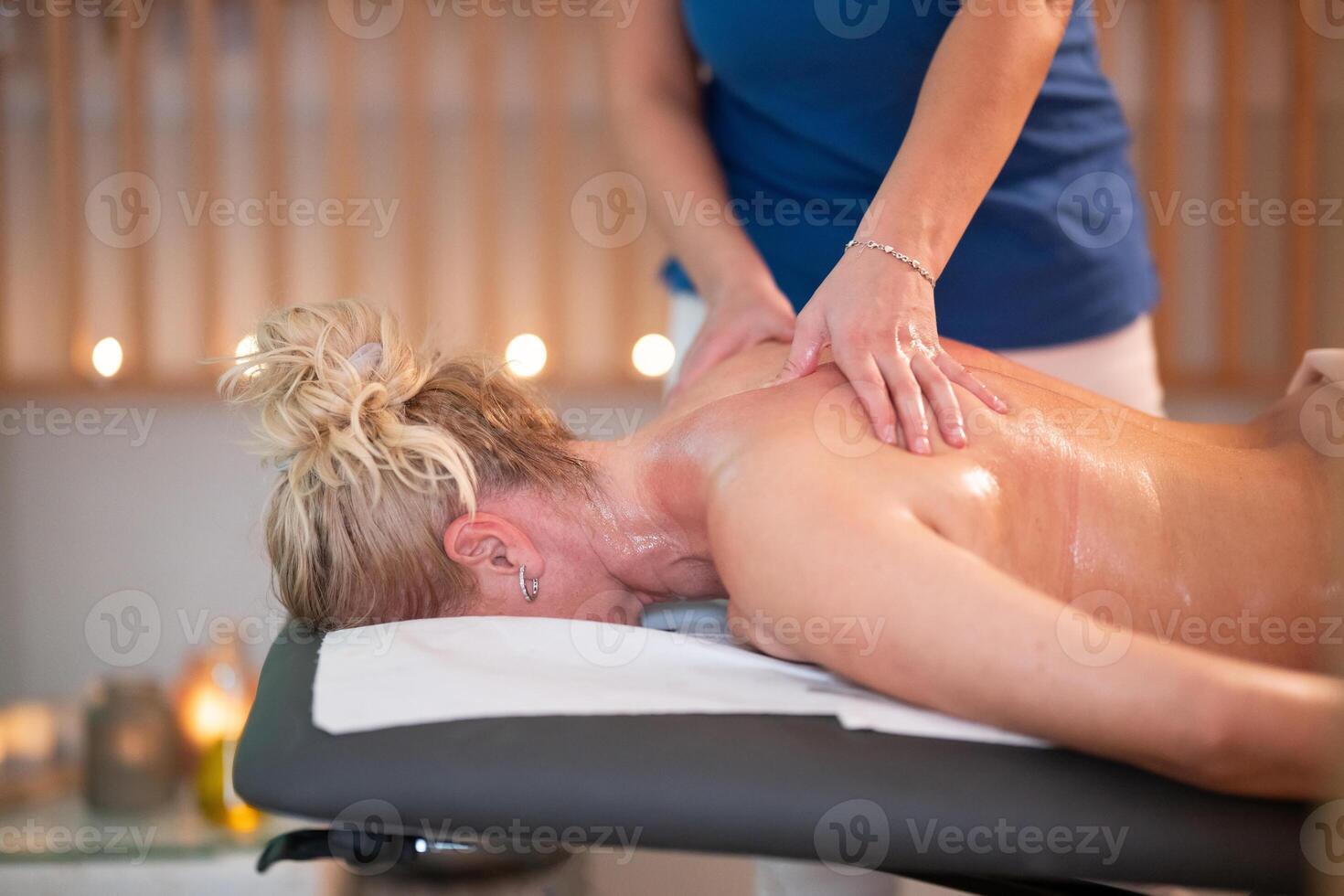Relaxing Back Massage in a Spa Setting. A professional massage therapist in a blue uniform provides a relaxing back massage to a client lying on a massage table. photo