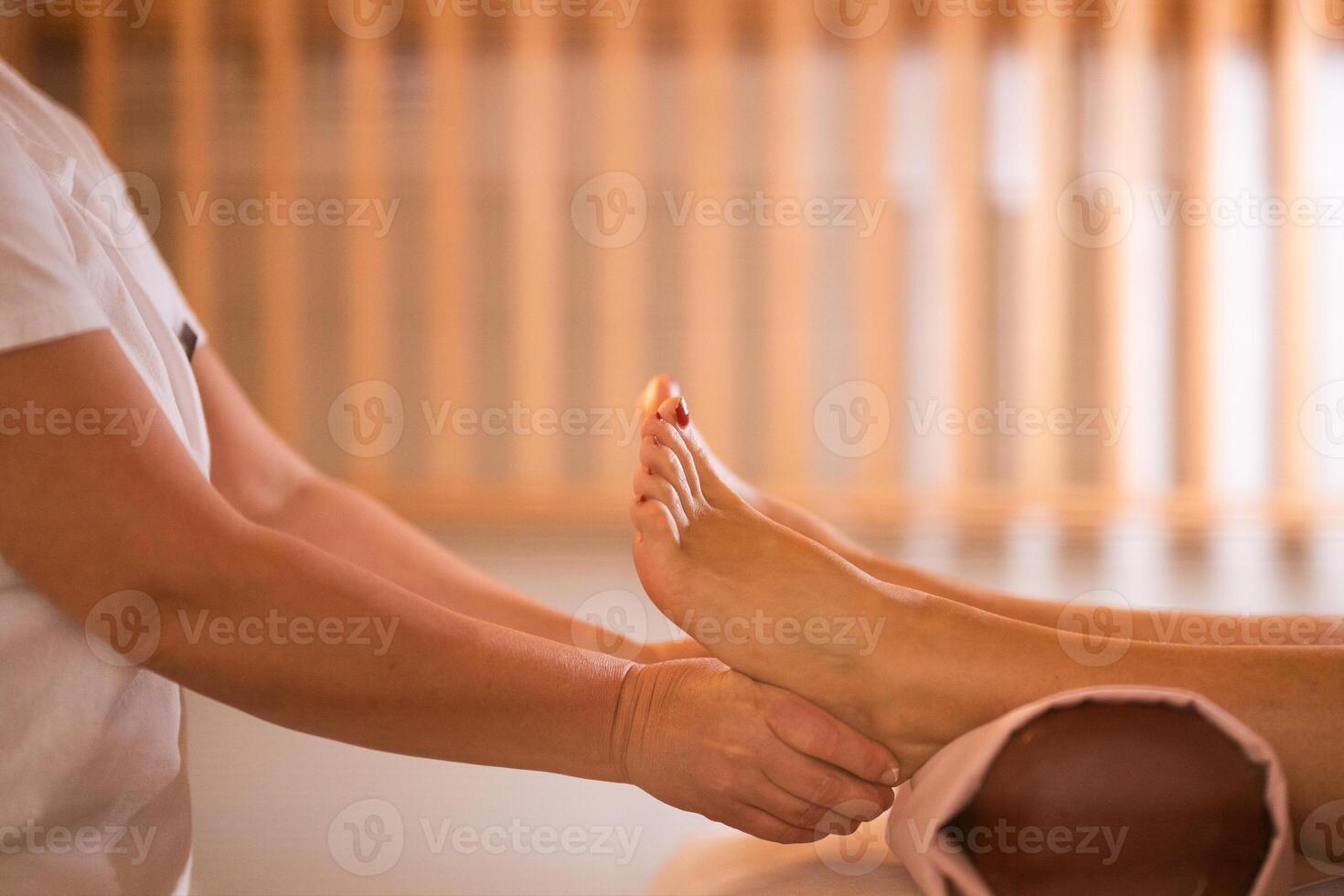 Foot Massage Therapy in a Relaxing Spa Setting. A professional massage therapist in a white uniform provides a soothing foot massage to a client in a calm and serene spa environment photo