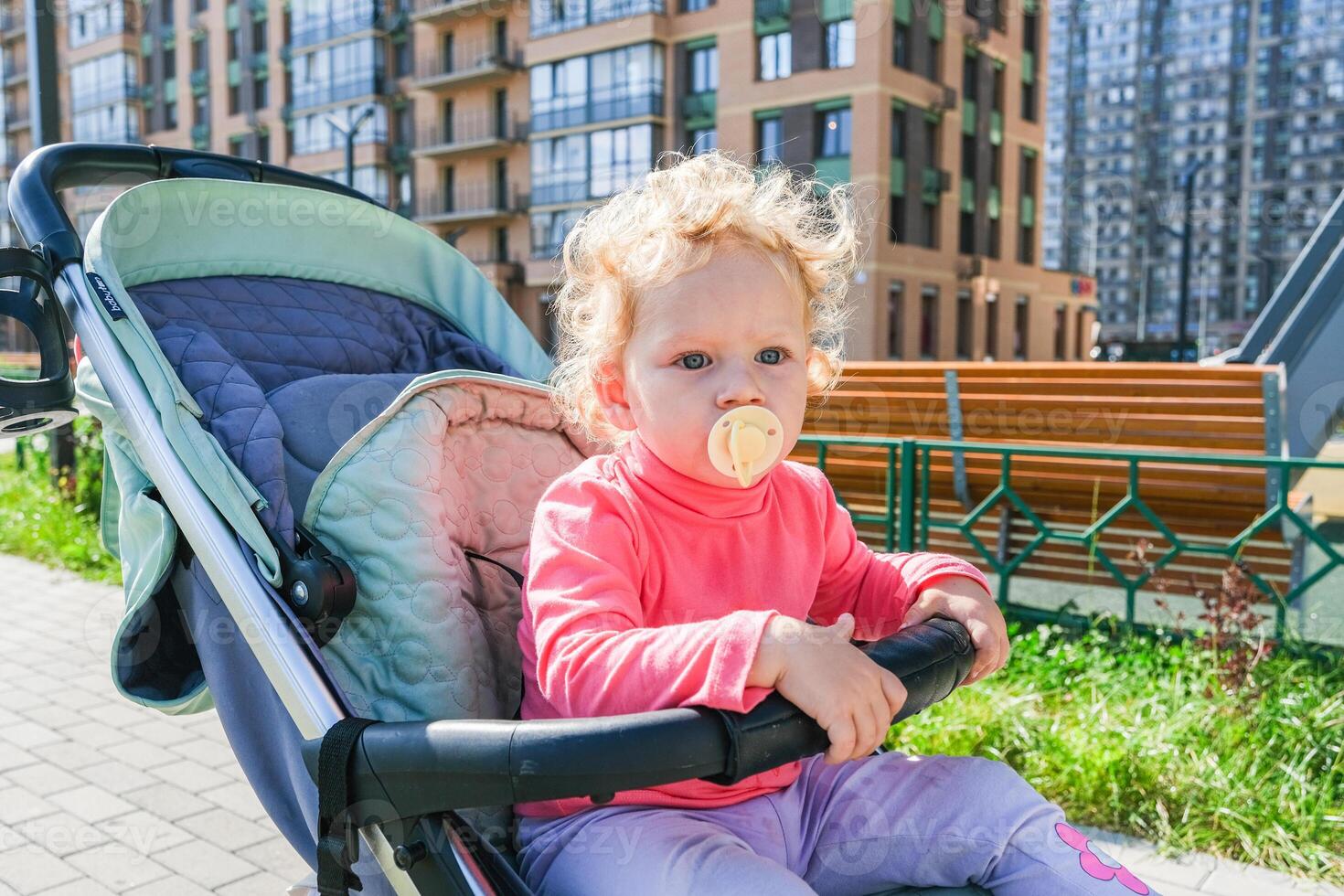 Girl with Wayward Curly Hair Sitting In Stroller And Sucking Pacifier photo