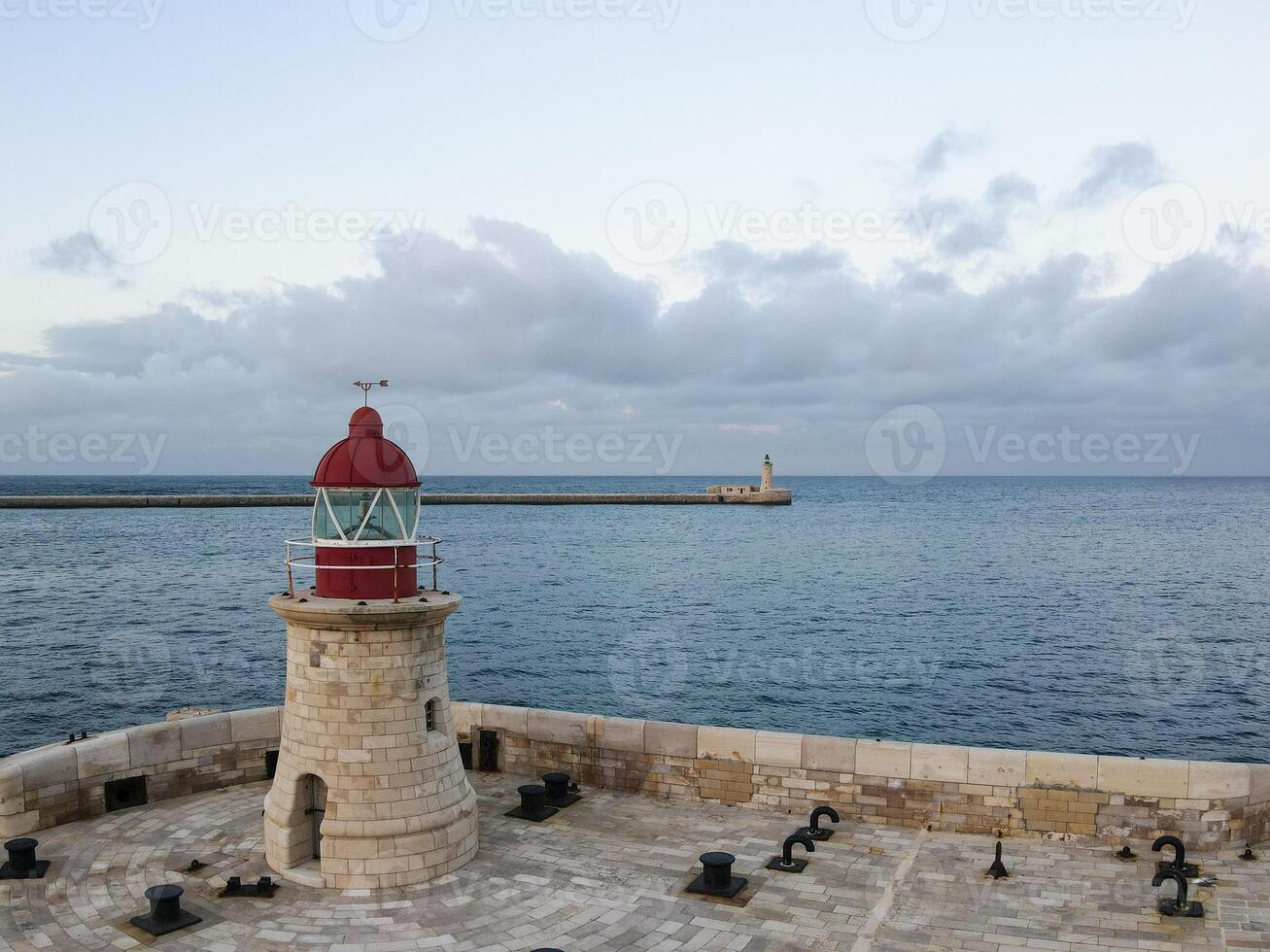 Scenic view of a red lighthouse on a stone pier with the ocean in the background. Maritime navigation and coastal landmark concept photo