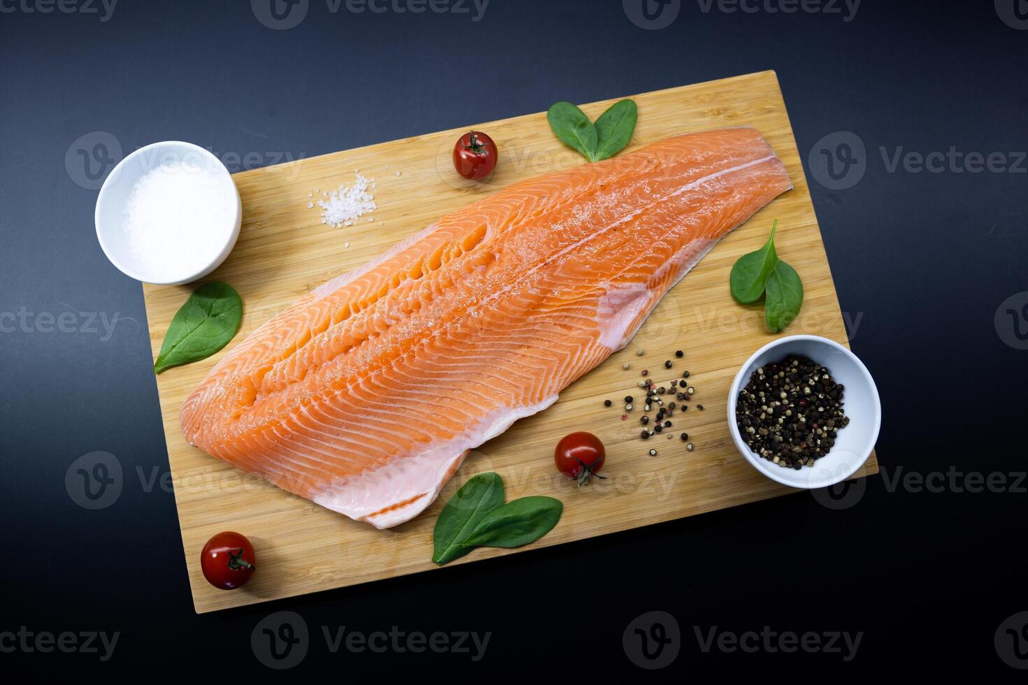 Fresh salmon fillet with seasoning ingredients on wooden board against dark background. Healthy eating and seafood preparation concept photo