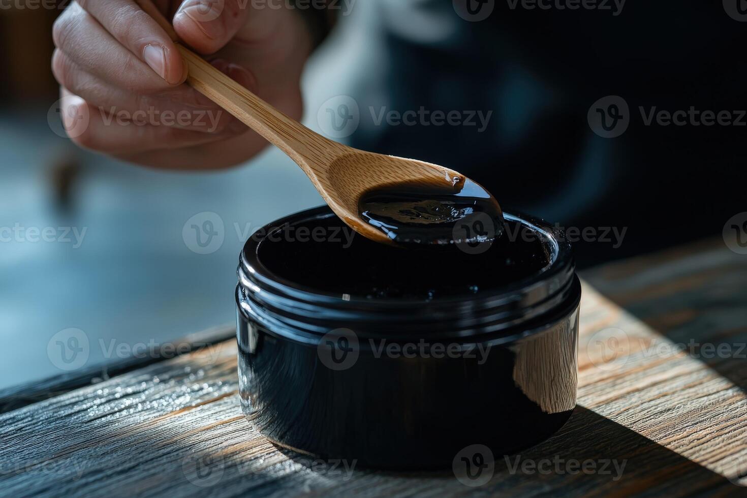 A person is holding a spoon over a jar of black paste photo