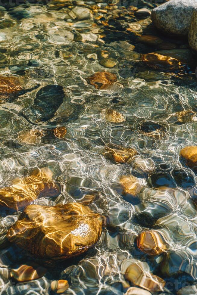 Clear river water reflecting light on smooth rocks below photo