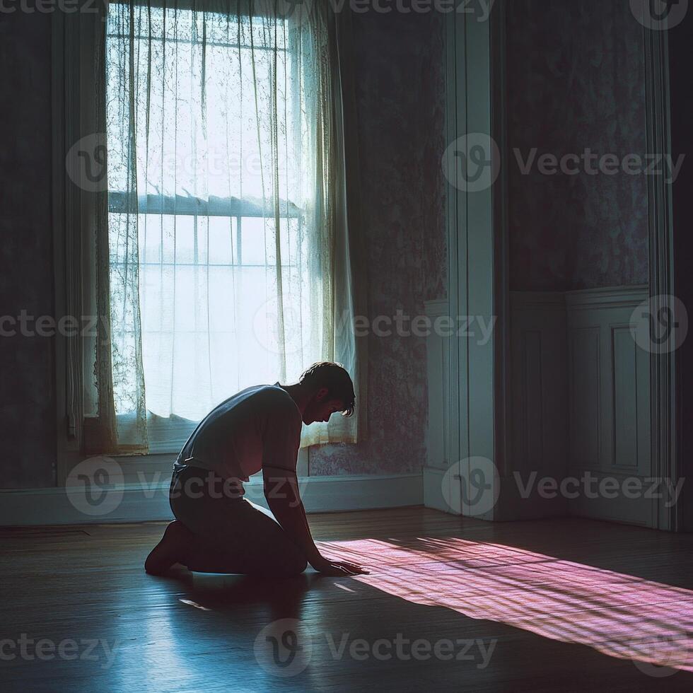 Man kneeling on floor in a sunlit room with sheer curtains photo