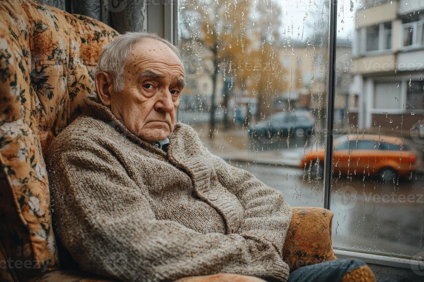 Elderly man sitting thoughtfully by a rainy window on a quiet afternoon in a cozy room photo