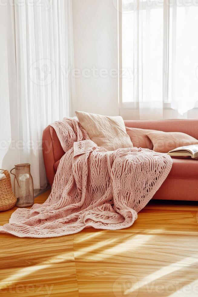 Cozy living room corner featuring a pink sofa adorned with a textured blanket and a warm atmosphere in natural light photo