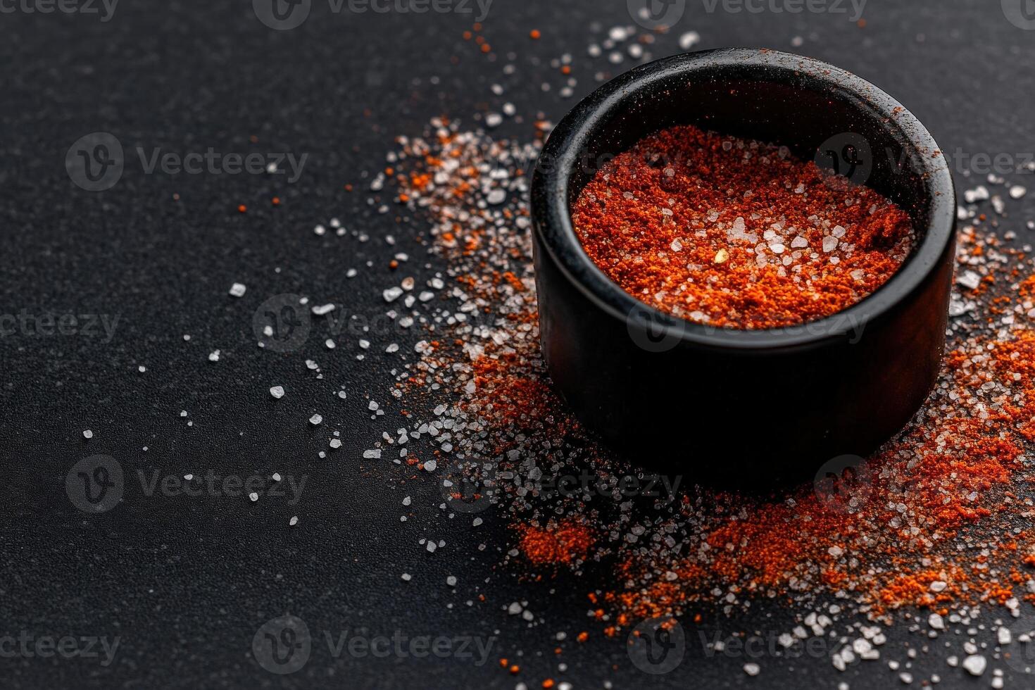 Spicy seasoning blend in a black bowl on a dark surface with contrasting salt granules surrounding it photo