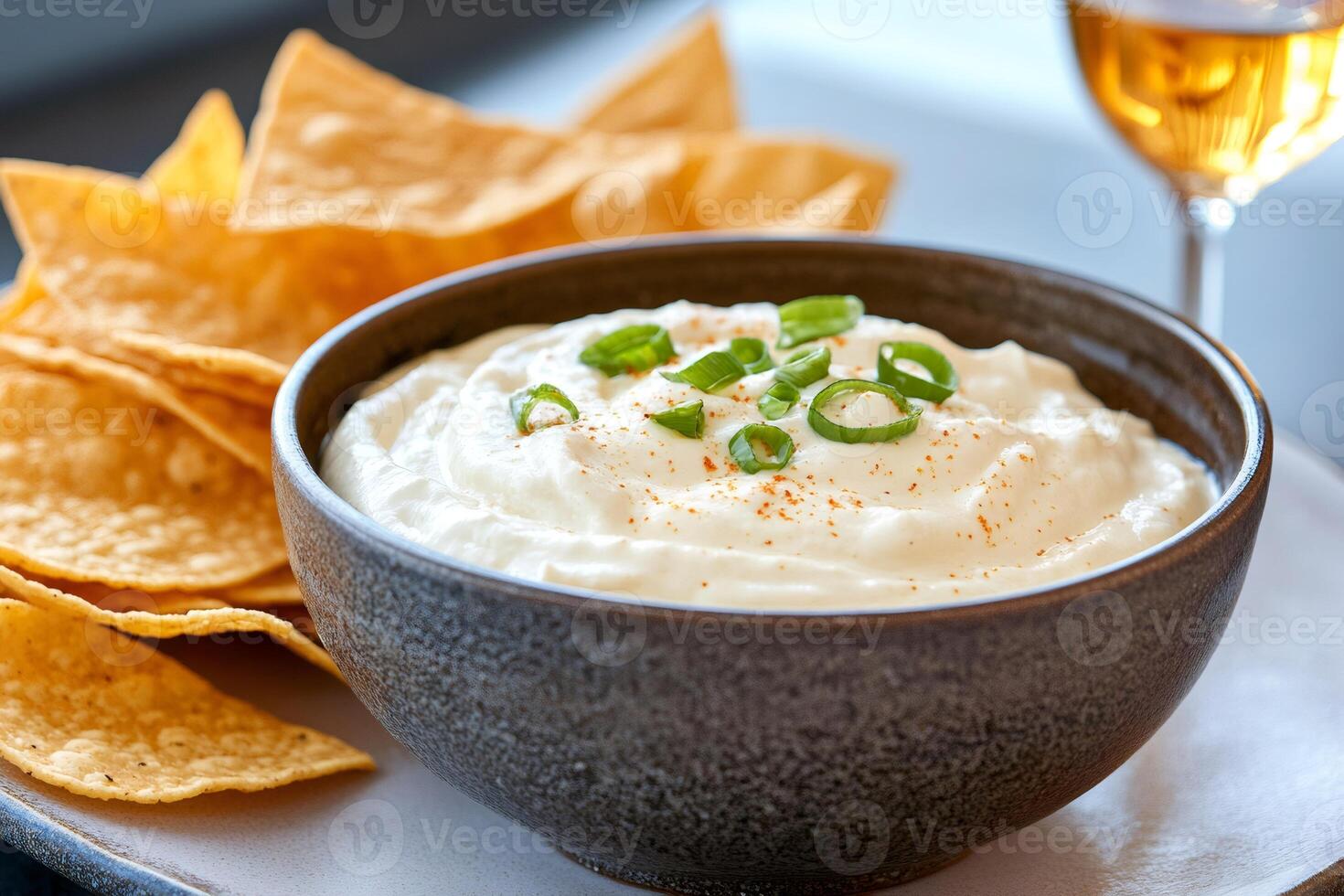 Creamy dip seasoned with chopped chives served with tortilla chips and white wine photo