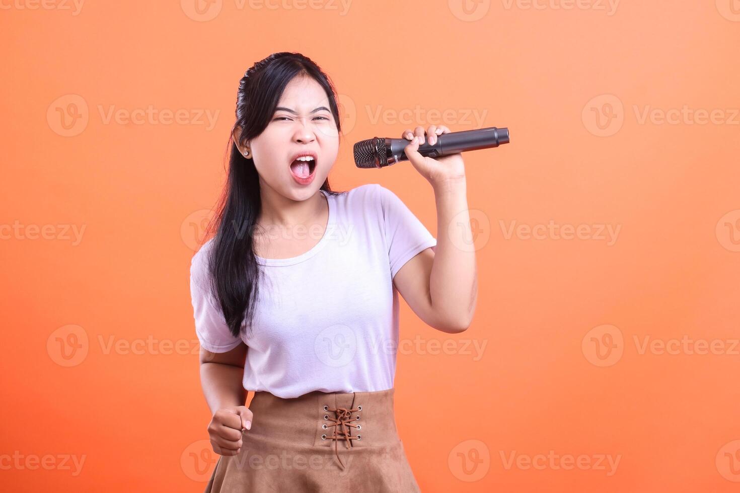 A young woman passionately sings into a microphone, expressing intense emotion and energy. She is a dynamic singer, isolated on orange background. photo
