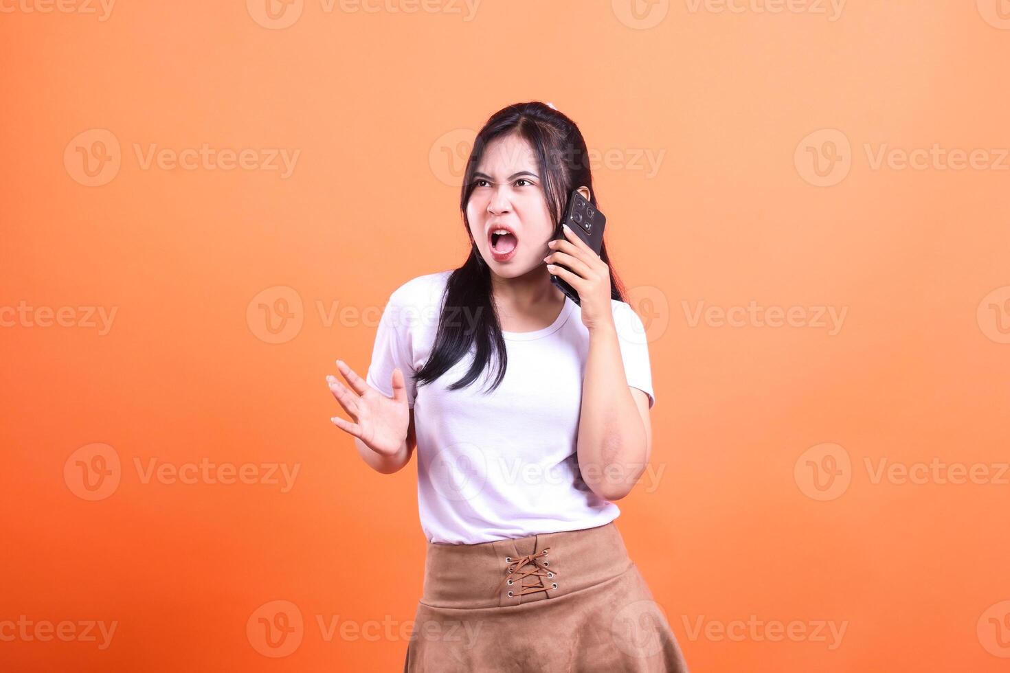 A woman with black hair yells on the phone with a bright orange background photo