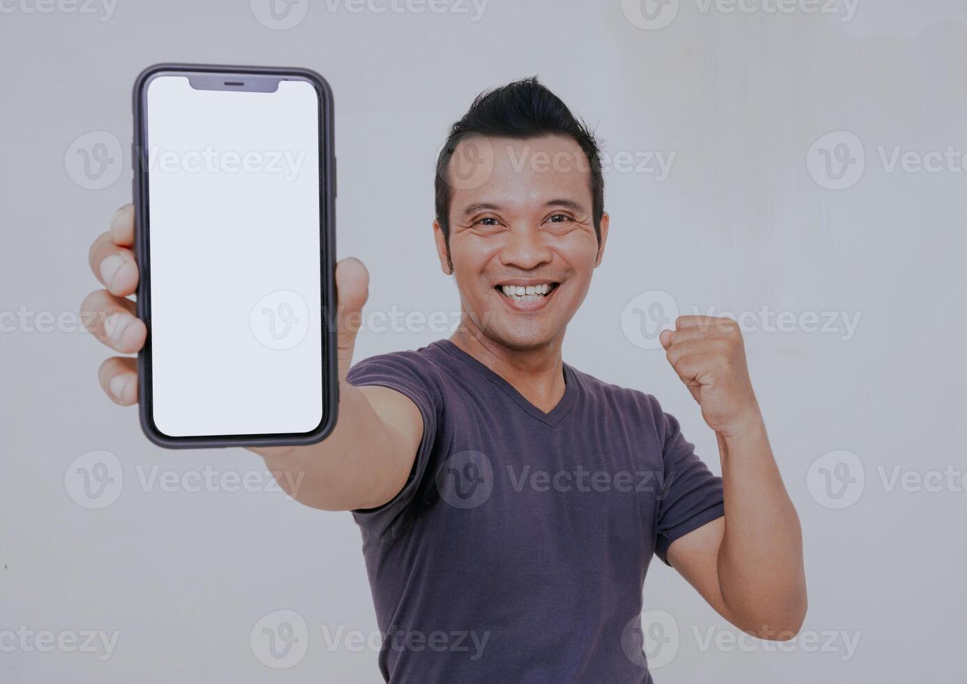 Portrait of excited asian man holding a smartphone with white blank screen in hand, showing close to camera and clenching fist. Gadget with empty free space for mock up and banner, isolated on white. photo