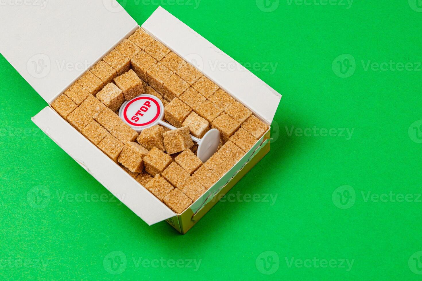 Stop sign surrounded by sugar cubes in a white box on bright green background photo