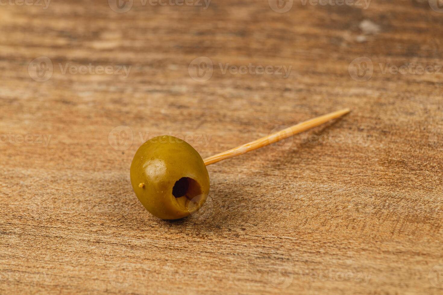 Enjoying a green olive on a toothpick resting on a wooden table photo