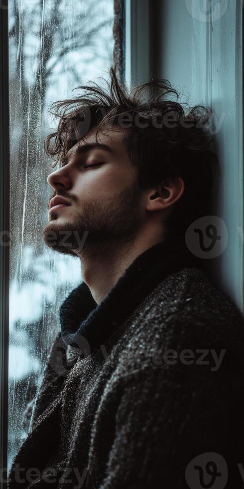 Lonely man sitting by the window lost in thought on a rainy day photo