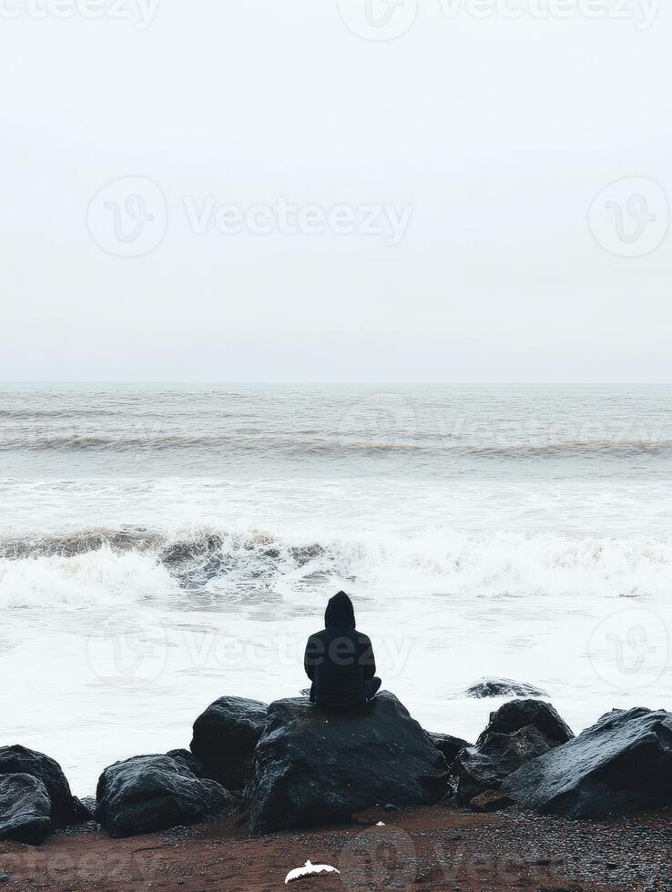 Person sitting on rocks by the ocean on a foggy day photo