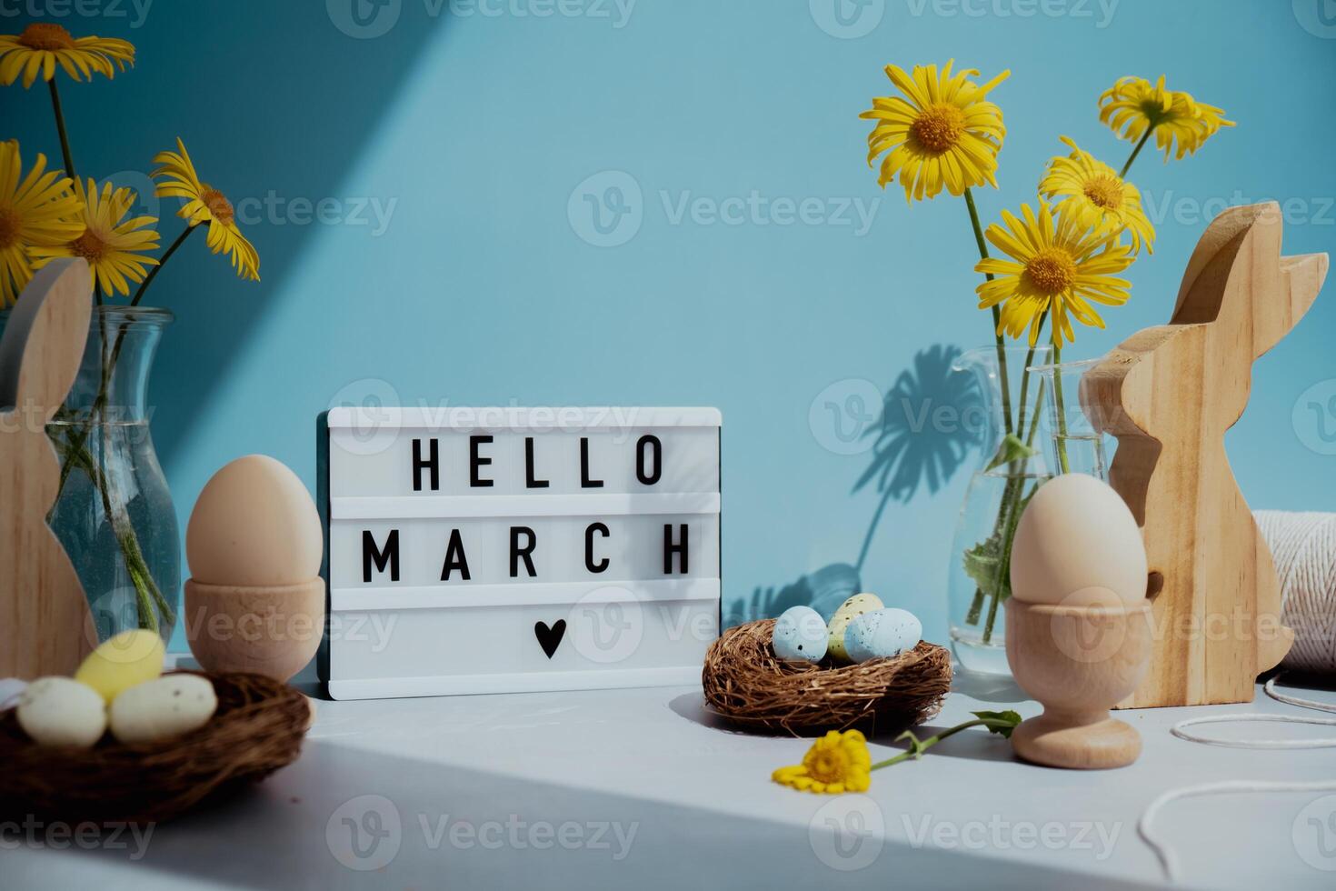 HELLO MARCH text on Lightbox with bunny wooden figures and fresh flowers. Easter composition content still life. Christian symbols of spring holiday photo