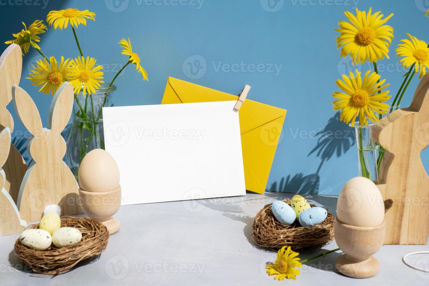 Empty white envelope mock up postcard copy space on festive blue background and eco-friendly zero waste natural decoration. Yellow daisies flowers. Bunny egg. Holiday greeting card photo