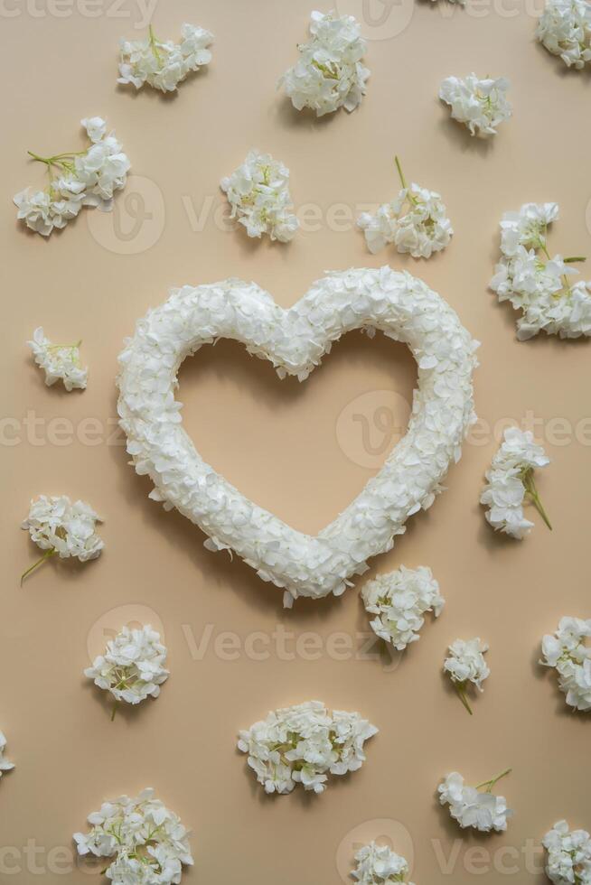 Heart made of white lilac flowers on pastel beige background. Still life romantic composition of Valentines day holiday copy space for your text invitation greeting card postcard. photo