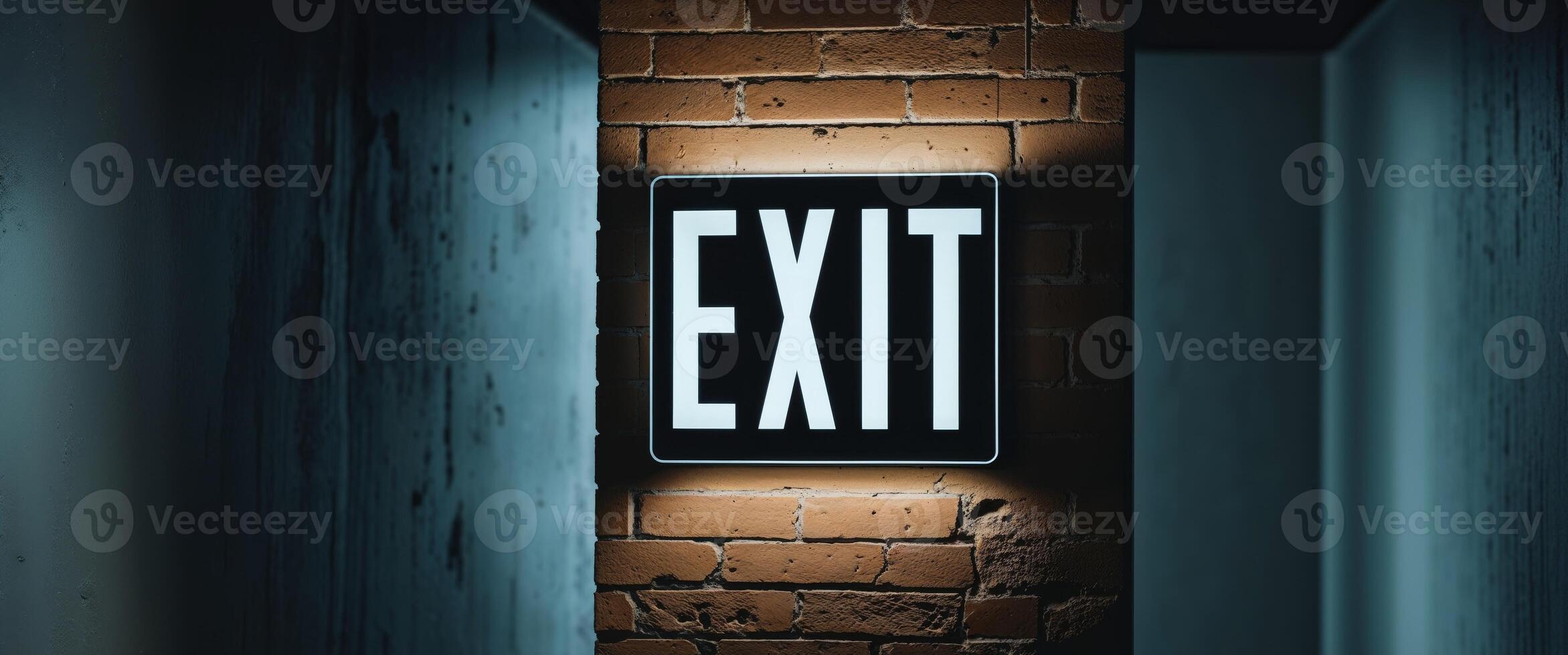 Bright exit sign glowing on a brick wall in a dimly lit corridor photo