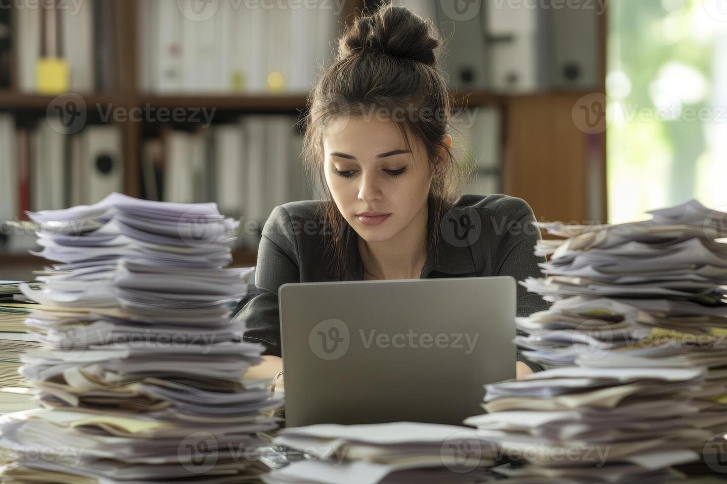 Woman Working at Desk with Laptop and Overwhelming Paperwork Stacks photo