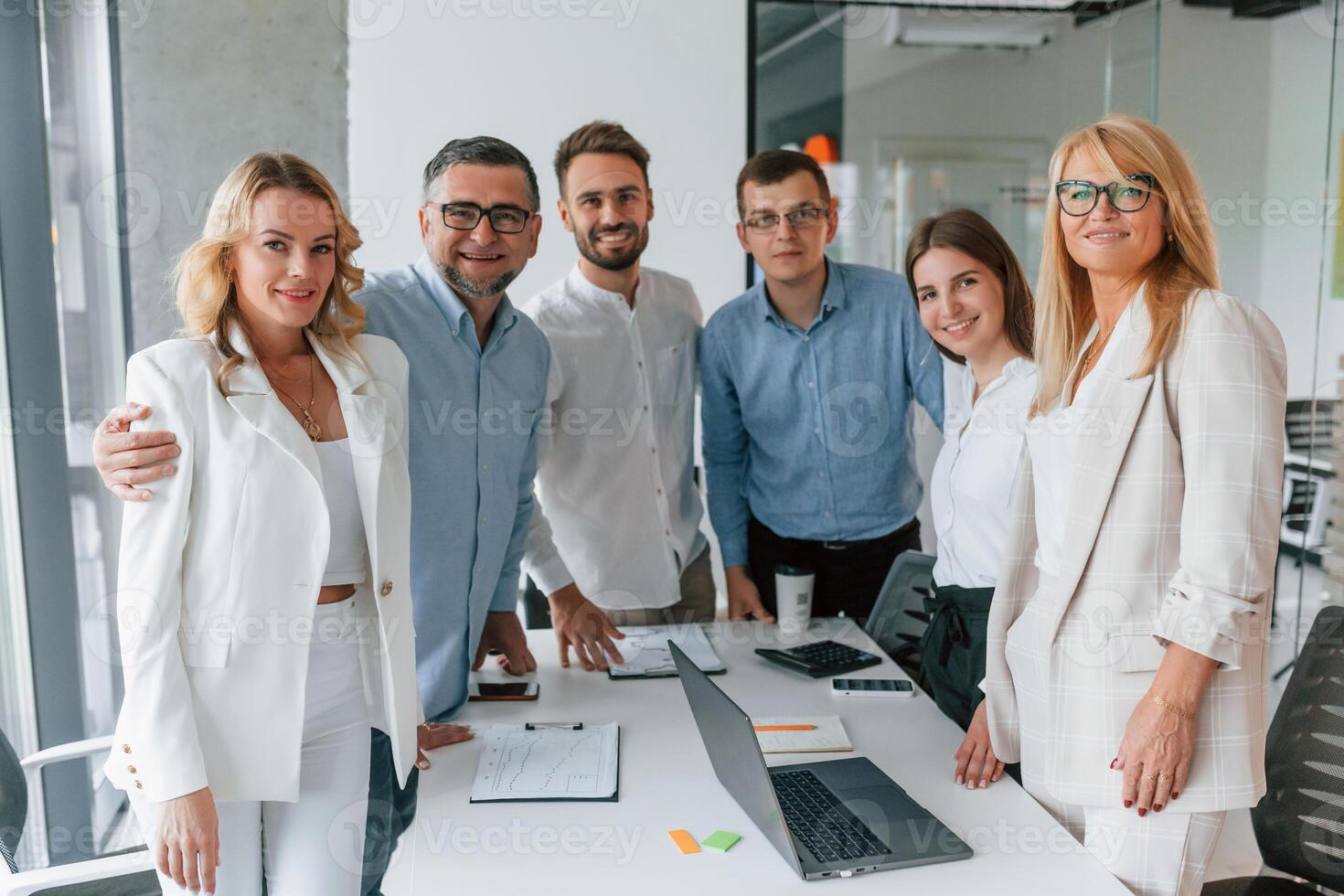 Standing together, looking into the camera and smiling. Group of professional business people is in the office photo