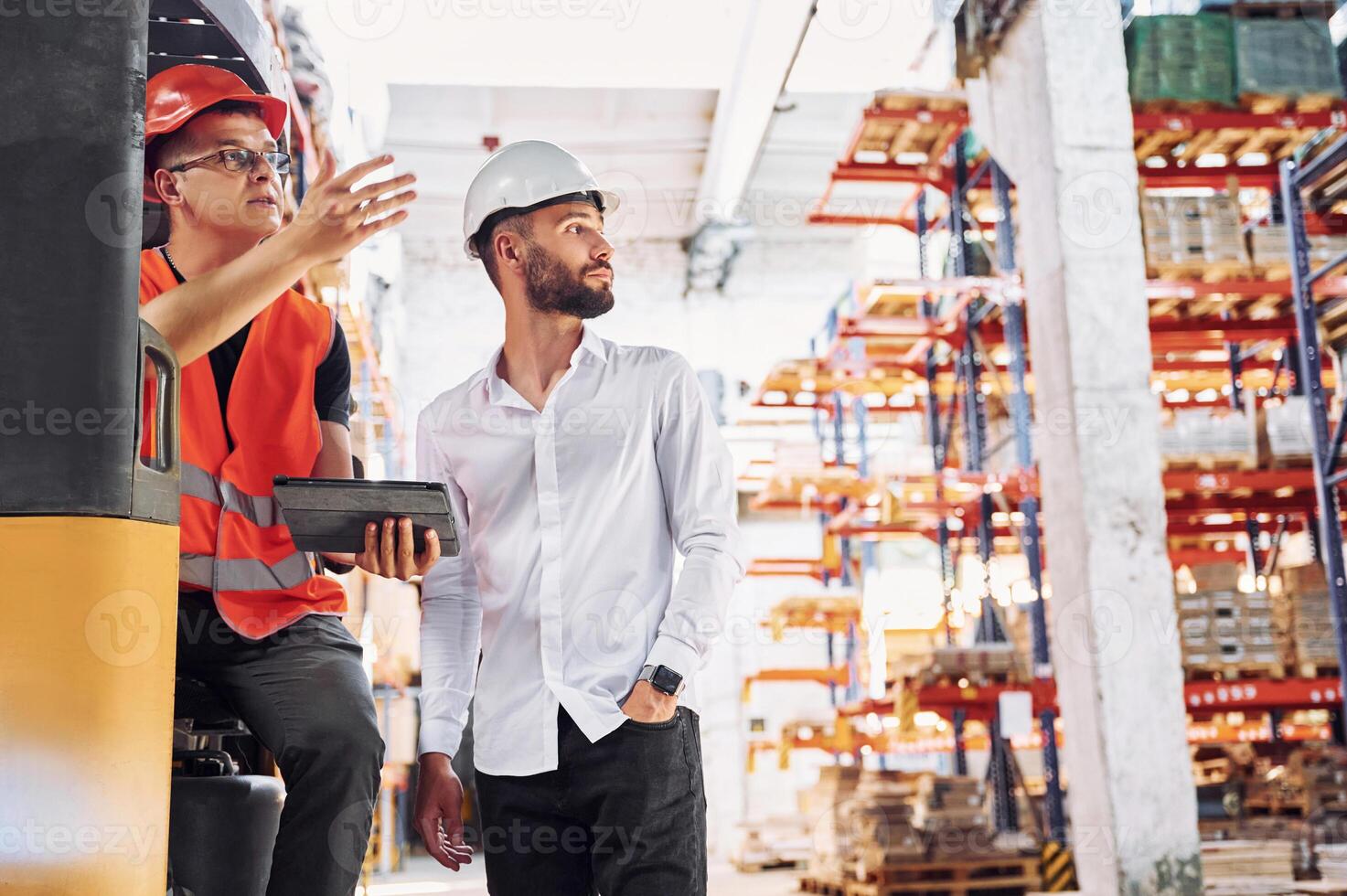 With tablet and cargo moving transport... Two storage workers is in the warehouse photo