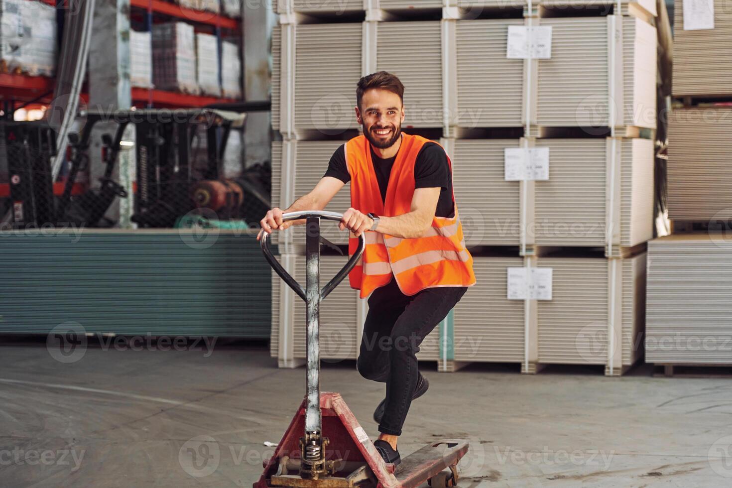 Standing with platform trolley. .Storage worker is in the warehouse with bunch of products photo