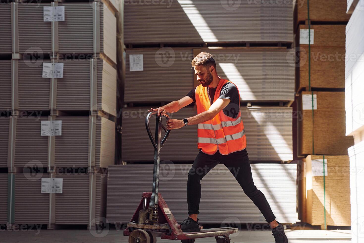 Riding the platform trolley. Storage worker is in the warehouse with bunch of products photo