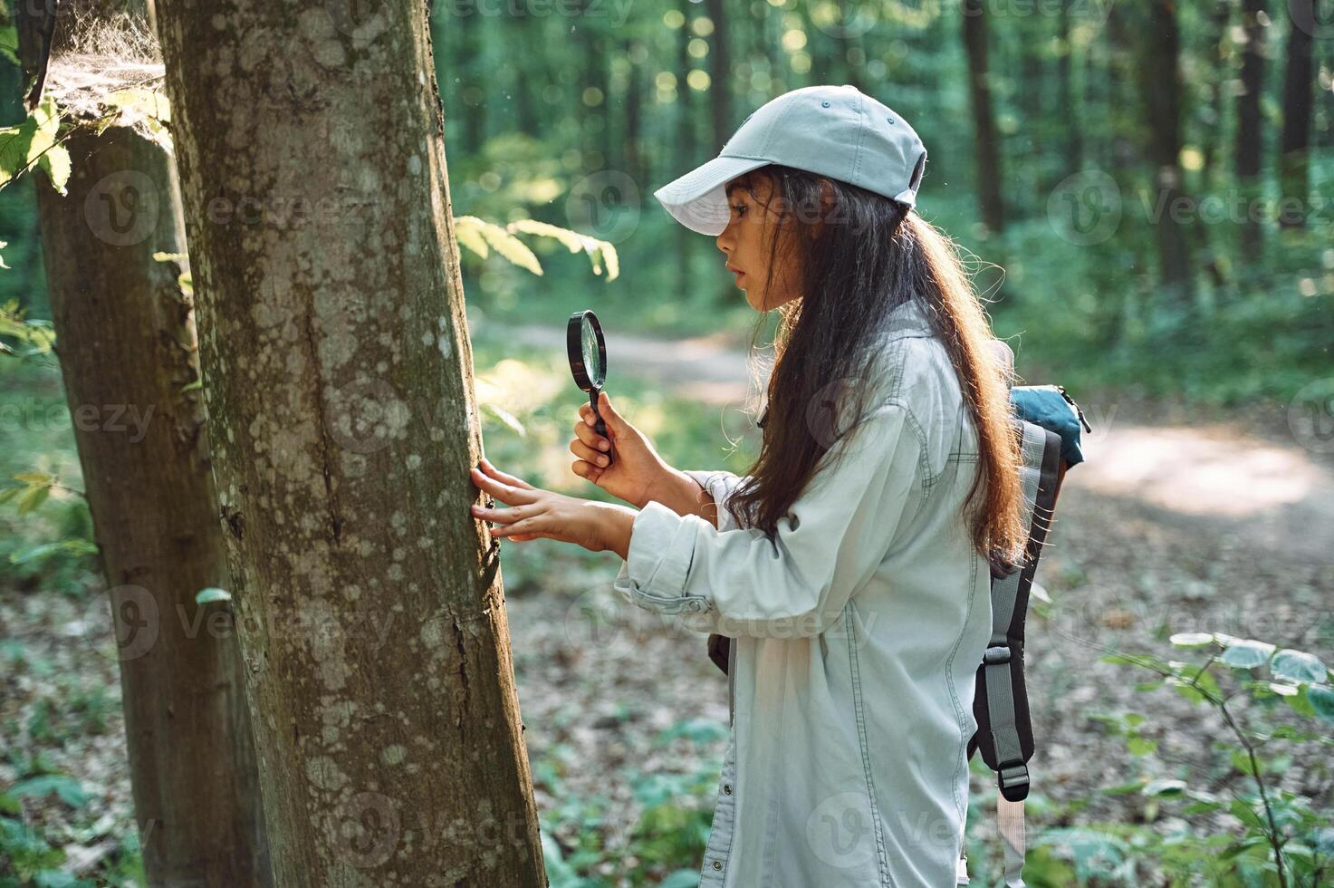 With magnifying glass.. Girl is in the forest at summer day time discovering new places photo