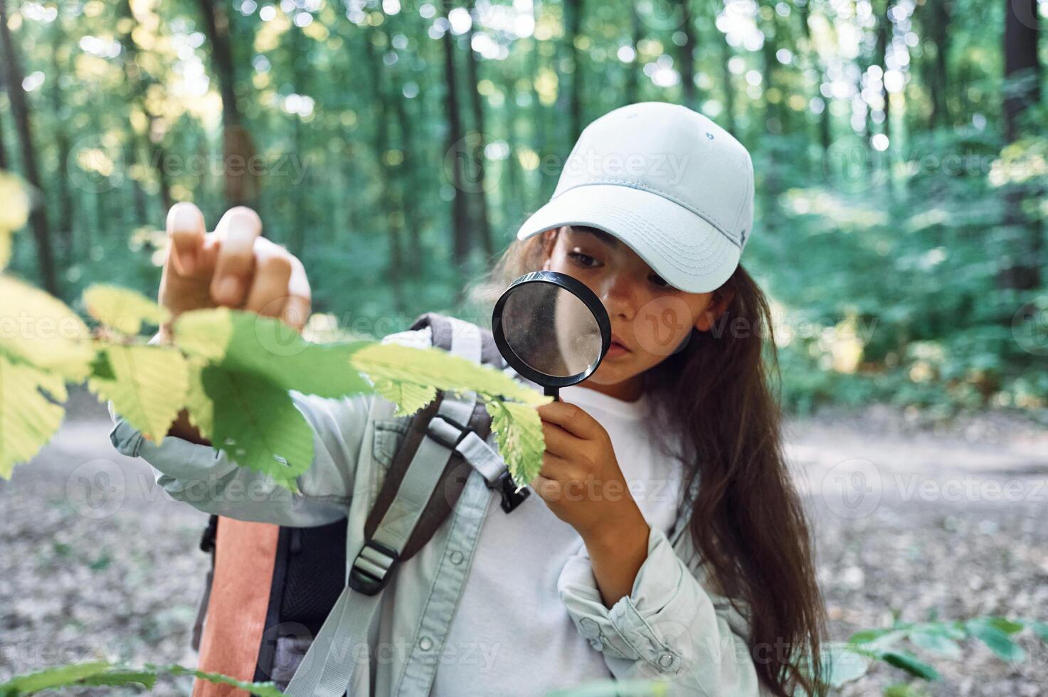 Using magnifying glass. Girl is in the forest at summer day time discovering new places photo