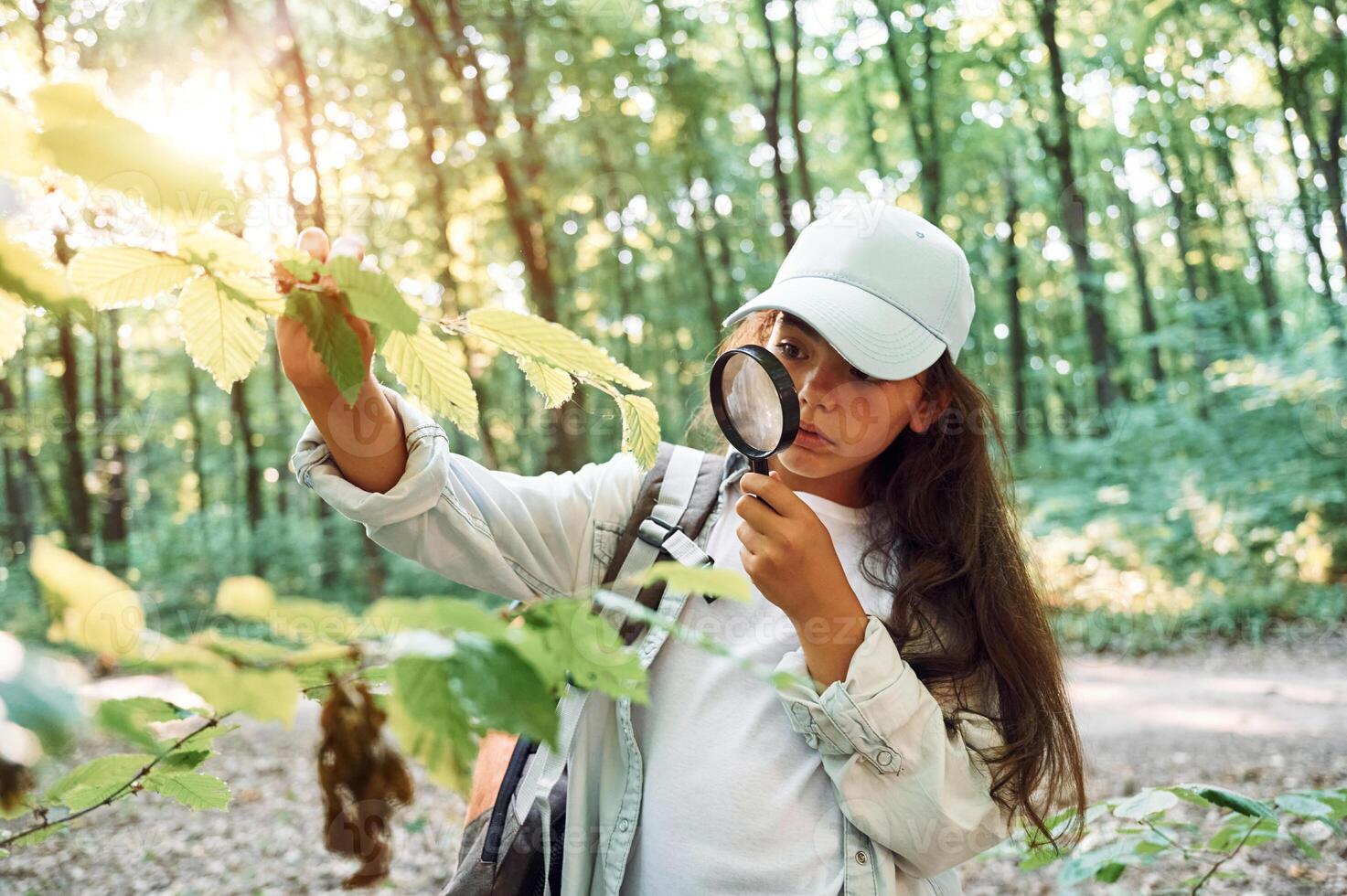 Using magnifying glass. .Girl is in the forest at summer day time discovering new places photo