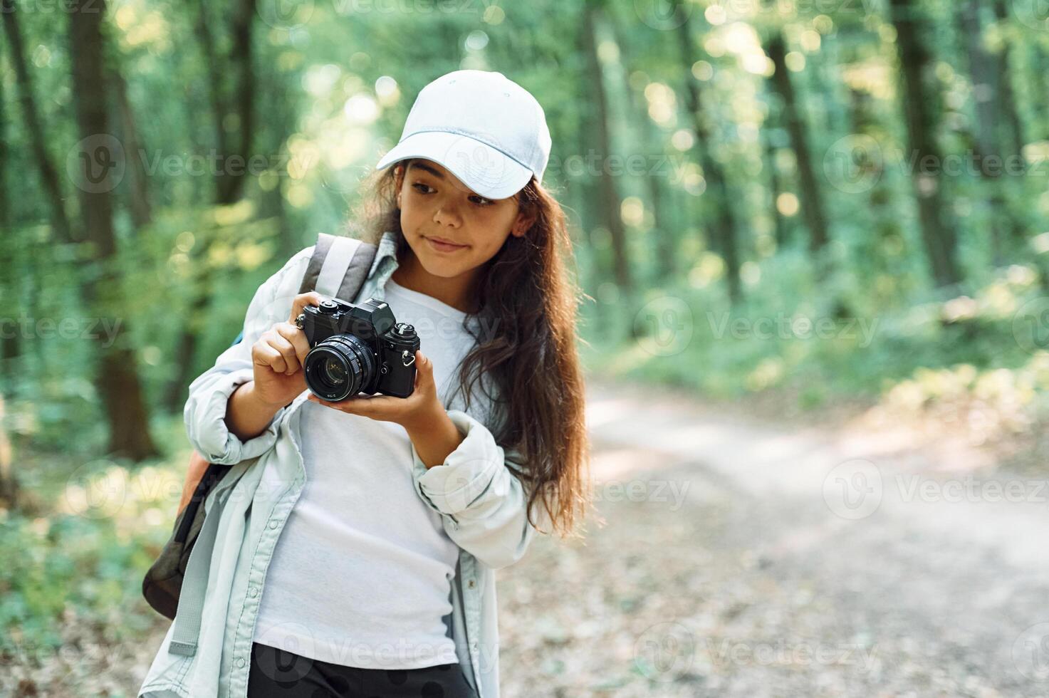 Standing and holding ,camera in hands. Girl is in the forest at summer day time discovering new places photo