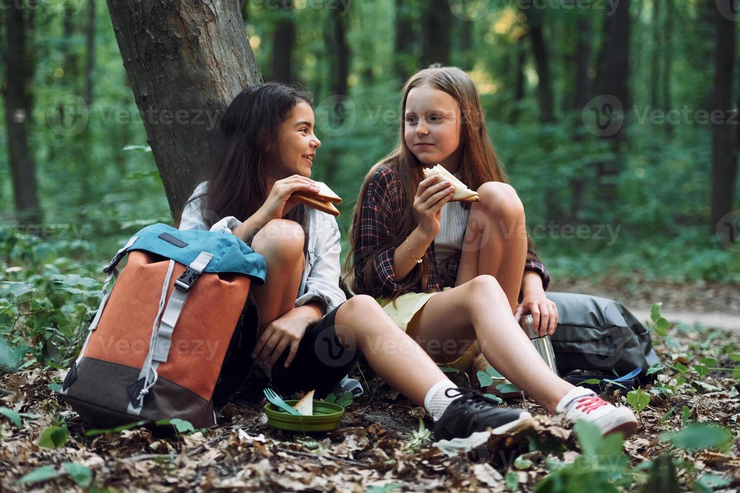 Eating .by using plastic forks and plates. Two girls is in the forest having a leisure activity, discovering new places photo