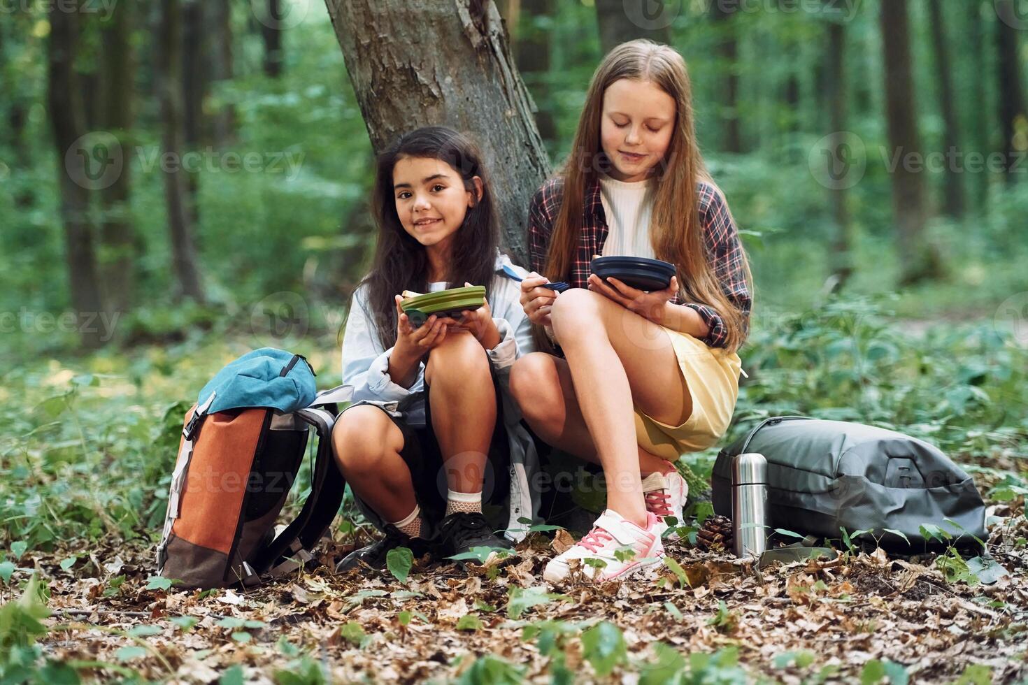 Eating by using plastic forks and plates. Two girls is in the forest having a leisure activity, discovering new places photo