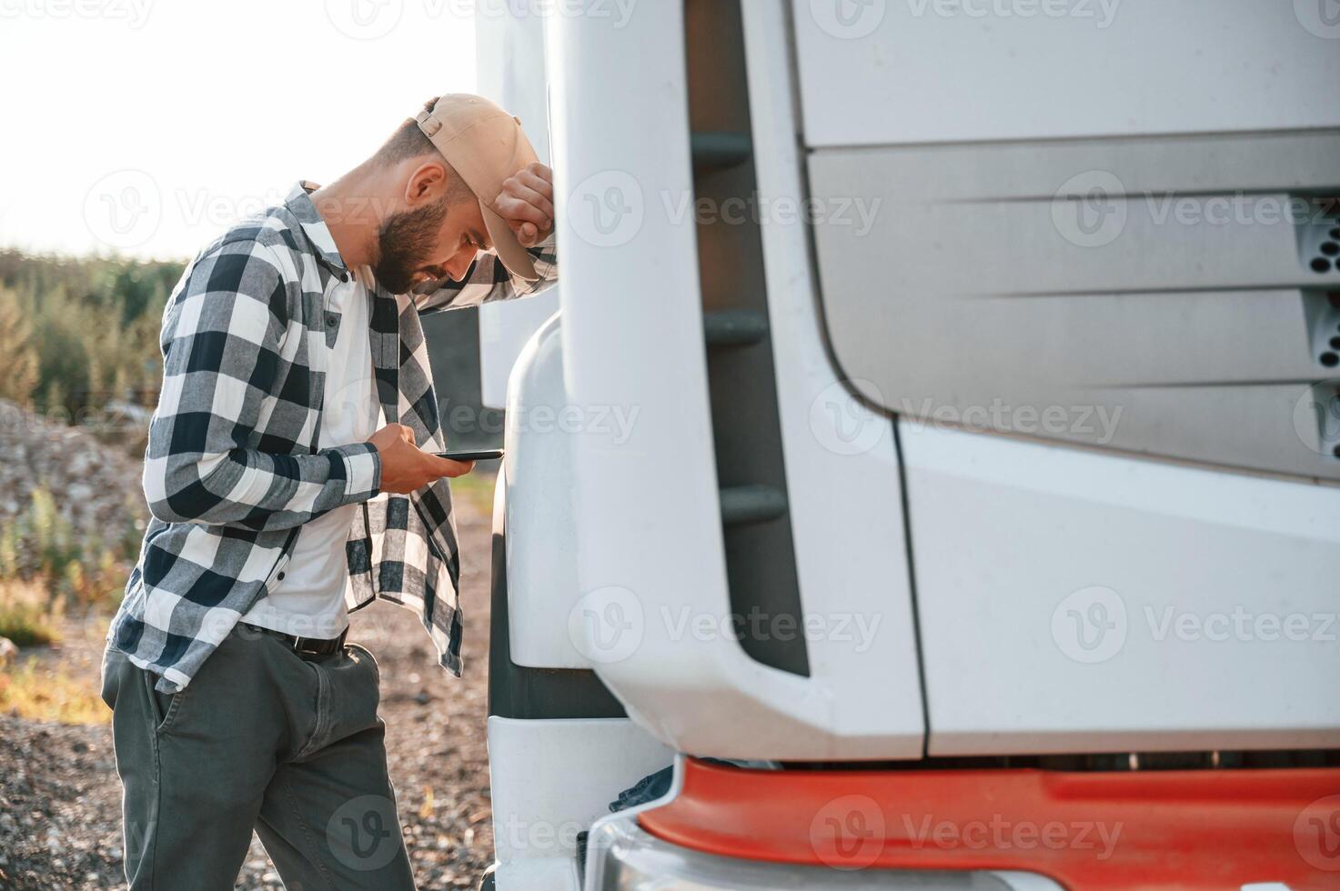 Feeeling tired. Using smartphone. Young truck driver is with his vehicle at daytime photo