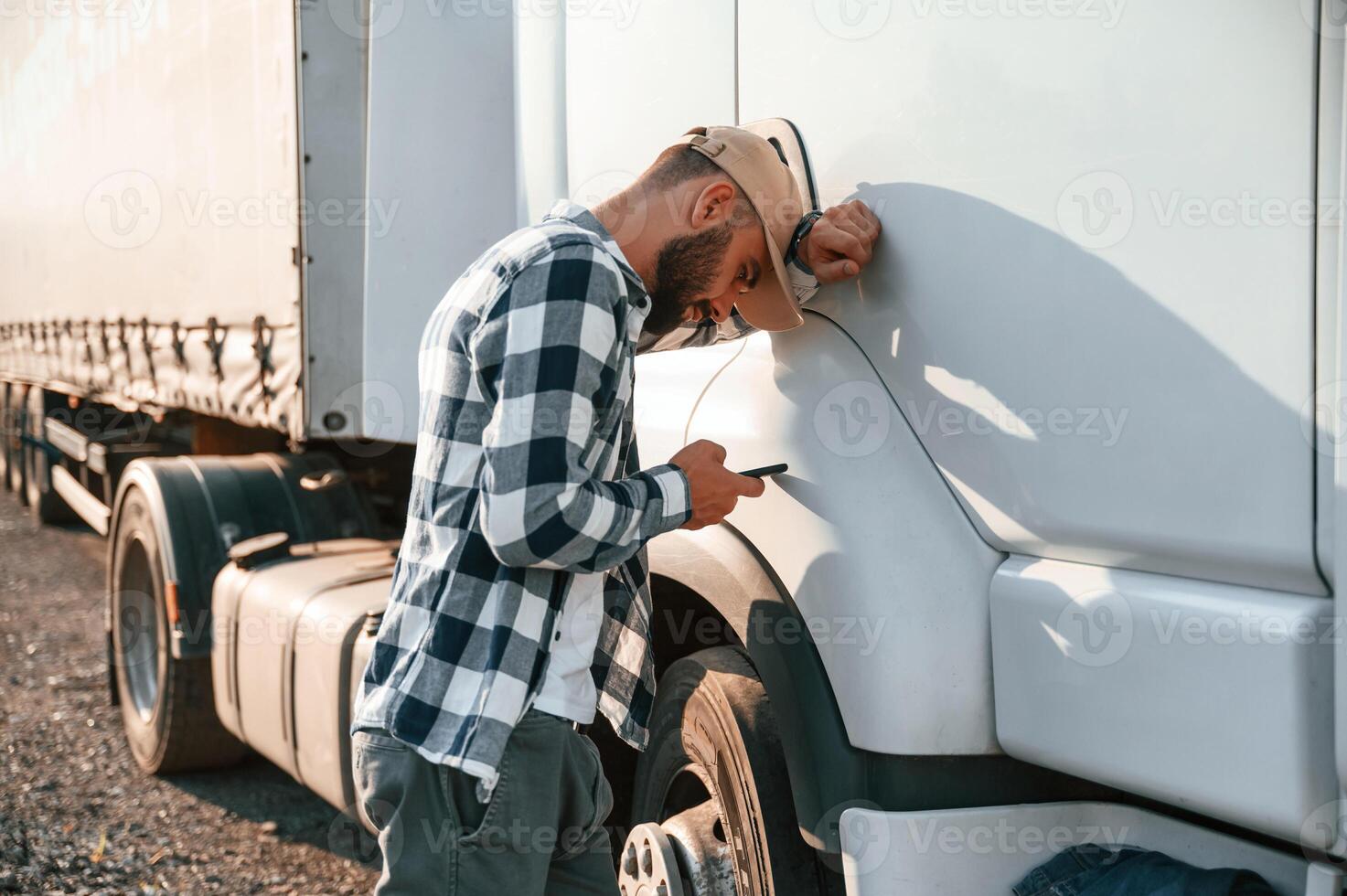 Feeeling tired. Using smartphone. Young truck driver is with his vehicle at daytime.. photo