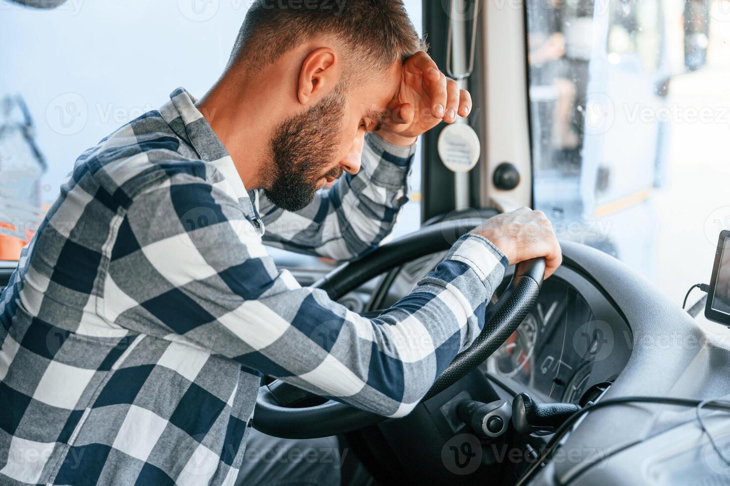 Tired of work. Sitting ,in the cabin. Young truck driver is with his vehicle at daytime photo