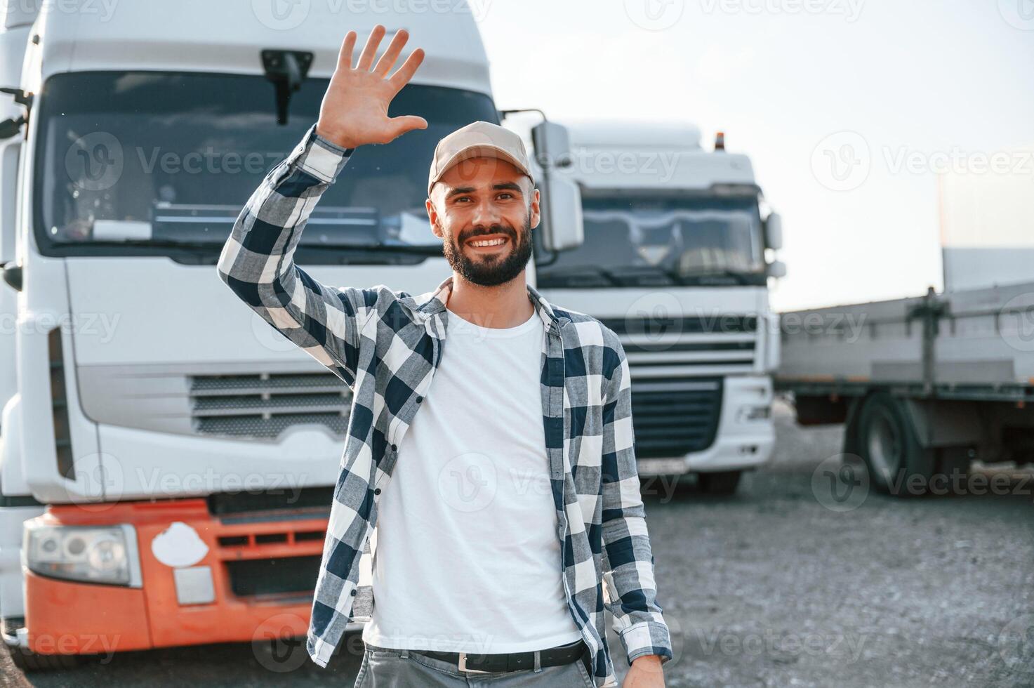 Showing hello gesture by hands and smiling. Young truck driver is with his vehicle at daytime photo