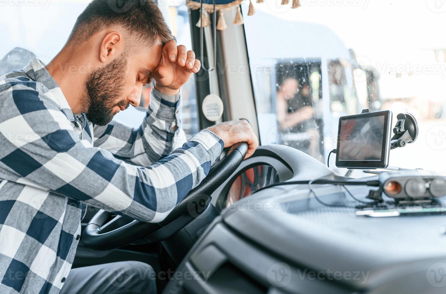 Tired of work. Sitting in the cabin. Young truck driver is with his vehicle at daytime photo