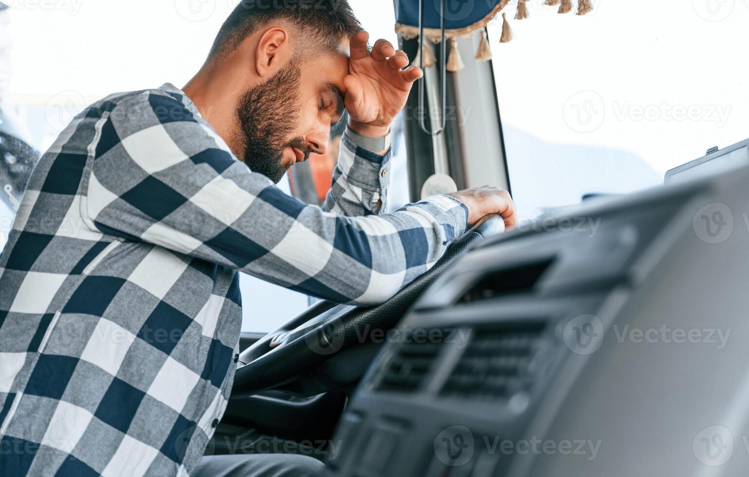 Tired of work. Sitting in the cabin. Young truck driver is with his vehicle at daytime. photo