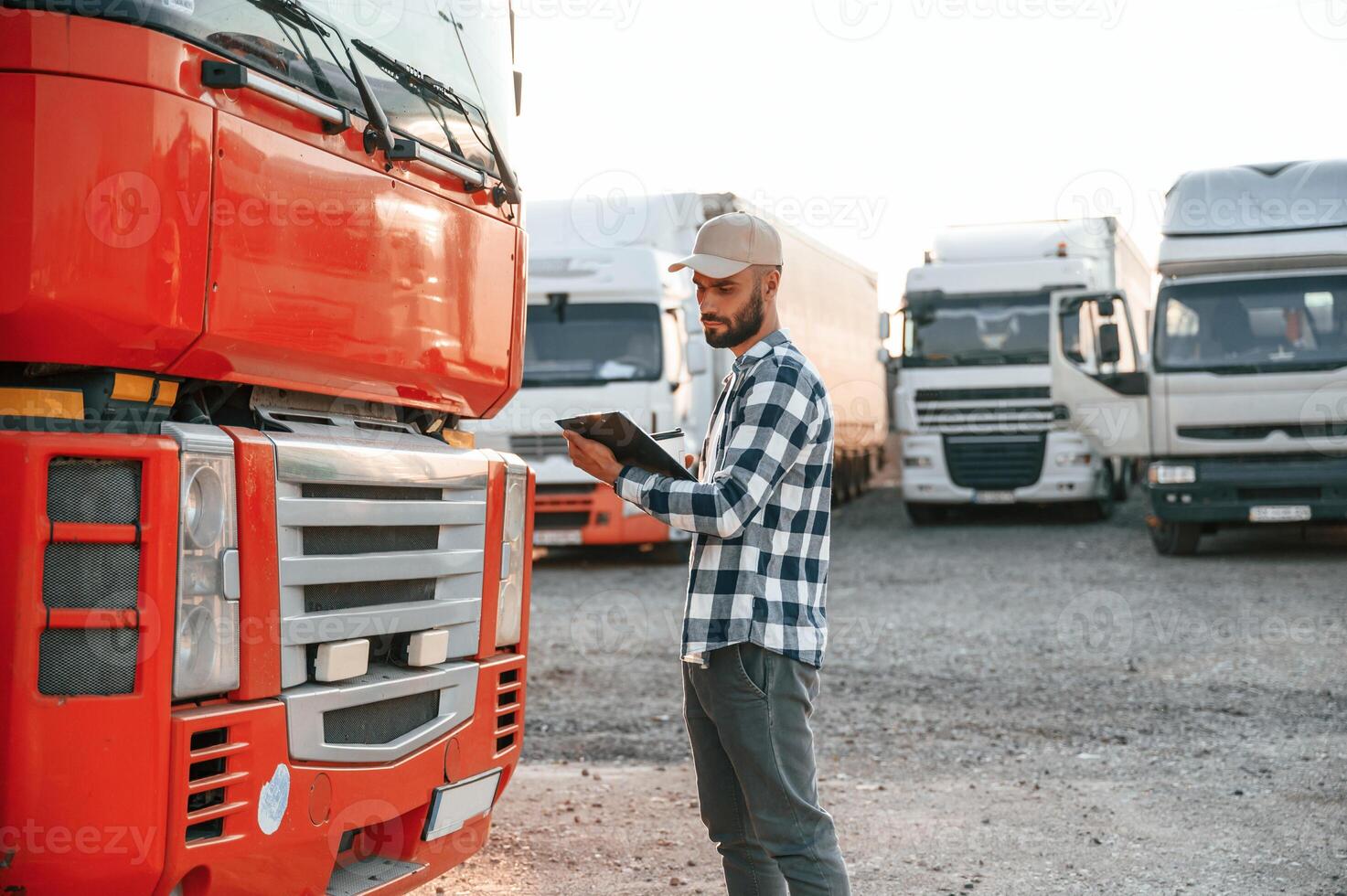 Looking at document in notepad. Young truck driver is with his vehicle at daytime photo