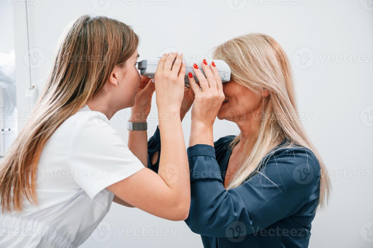 Woman's vision is tested by clinic worker that using special device photo
