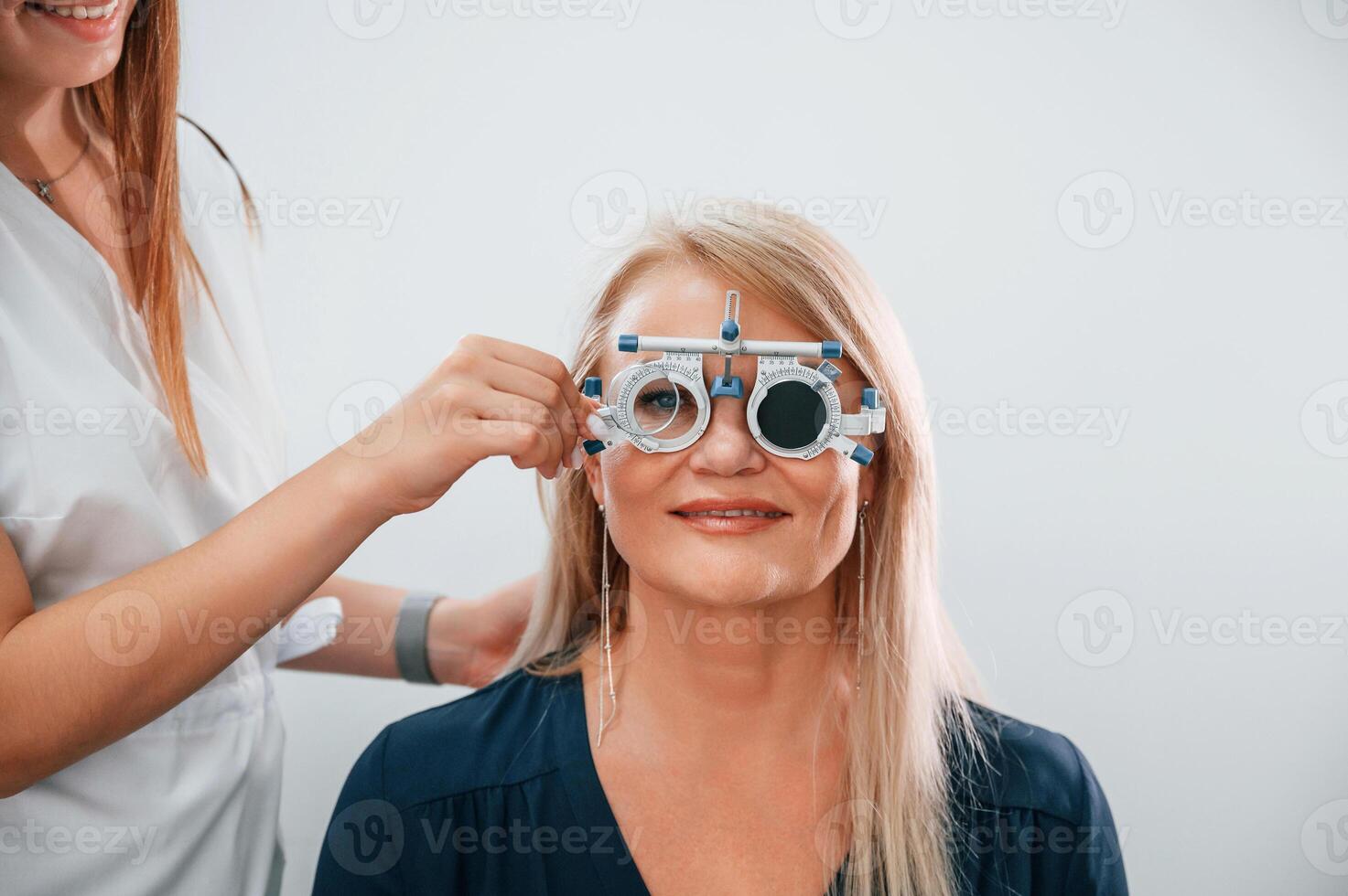 Wearing glasses. Woman's vision is tested by clinic worker that using special device photo